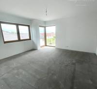 Ein leerer Raum mit grauem Boden und zwei Fenstern in einem Einfamilienhaus.