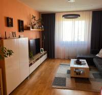 Wohnzimmer mit einer orangefarbenen Wand, dunklen Vorhängen, einem großen Fenster und Möbeln in einer 3-Zimmer-Wohnung.