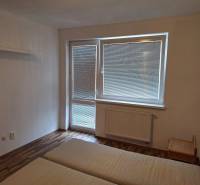 Schlafzimmer in einer Zweizimmerwohnung mit Bett und Fenster mit Jalousien.