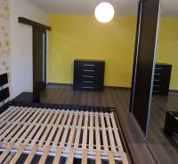 Schlafzimmer in einer 2-Zimmer-Wohnung mit Bett, zwei Kommoden und gelber Wand.