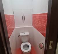 Toilette mit weißen Fliesen und einem Schrank in einer Zweizimmerwohnung mit roten Fliesen.