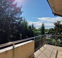 Der Balkon eines Einfamilienhauses mit Blick auf Bäume, sonniger Tag, offene Türen.