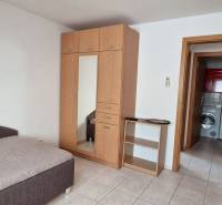 Ein Zimmer in einem Einfamilienhaus mit einem Bett, einem Schrank und einem Blick ins Badezimmer mit einer Waschmaschine.