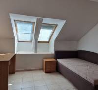Ein Dachzimmer in einem Einfamilienhaus mit zwei Dachfenstern, einem Bett und einem Schreibtisch.