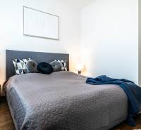 Schlafzimmer in einer 2-Zimmer-Wohnung mit einem bequemen Bett, einer Tischlampe und dekorativen Kissen.