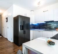 Küche in einer 2-Zimmer-Wohnung mit weißen Schränken, einem schwarzen Kühlschrank und Holzboden.