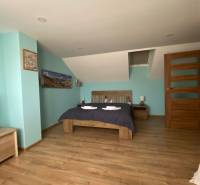 Einfamilienhaus: Schrägdach, Ehebett, Holzboden, blaue Wand und Nachttische.