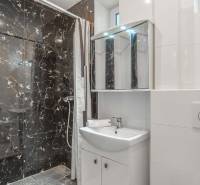 Badezimmer in einer 2-Zimmer-Wohnung mit dunklen Marmorkacheln und einer Duschkabine.