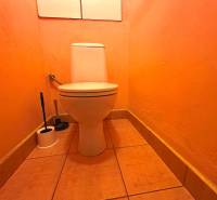 Oranges WC in einer 3-Zimmer-Wohnung mit einer Toilettenbürste in der Ecke des Raumes.