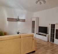 Wohnzimmer in einer 2-Zimmer-Wohnung mit beigem Sofa und Fernseher auf einem weißen Schrank.