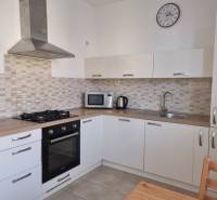 Küche mit weißen Schränken, Dunstabzugshaube und Geräten in einer 2-Zimmer-Wohnung.
