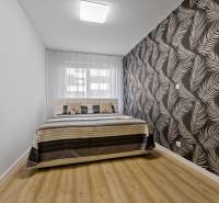 Schlafzimmer mit Bett und gemusterten Tapeten in einer 2-Zimmer-Wohnung.