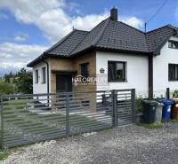 Ein Einfamilienhaus in Liptovský Hrádok mit modernem Schrägdach und Tor, daneben stehen Mülltonnen.