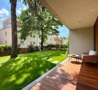 Terrasse mit Garten bei einer 4-Zimmer-Wohnung, Bäume und Gebäude im Hintergrund.