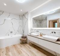 Badezimmer mit Badewanne und Doppelwaschbecken in einer 4-Zimmer-Wohnung, Marmorwände und Holzboden.