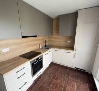 Küche in einer 2-Zimmer-Wohnung mit Holzschränken und dunklen Fliesen.
