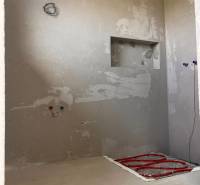 Badezimmerbaufläche in einem Einfamilienhaus, man sieht die Leitungen und eine Nische an der Wand.