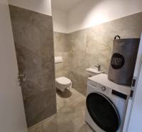 Badezimmer mit grauen Fliesen, Waschmaschine und Wäschekorb in einer 3-Zimmer-Wohnung.