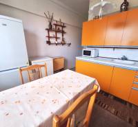 Küche in einer 2-Zimmer-Wohnung mit orangefarbener Küchenzeile, weißem Kühlschrank und Esstisch.