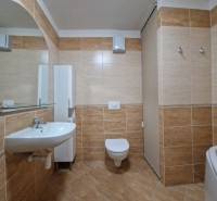 Badezimmer in einer Ferienwohnung mit Waschbecken, Spiegel und Toilette, gefliest mit braunen Fliesen.