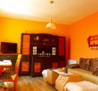 Wohnbereich in der Hütte mit orangefarbenen Wänden, Sofa und Fernseher.