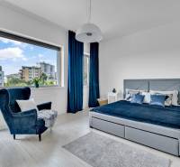 Helles Schlafzimmer in einer 4-Zimmer-Wohnung mit großem Fenster, blauen Vorhängen und einem bequemen Sessel.