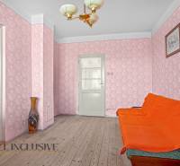 Ein Zimmer in einem Einfamilienhaus mit einem orangefarbenen Sofa, rosa Tapete und einer Vase auf dem Holzboden.