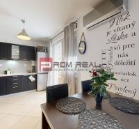 Esszimmer und Küche in einer Zweizimmerwohnung mit dunklen Möbeln und dekorativem Schriftzug an der Wand.