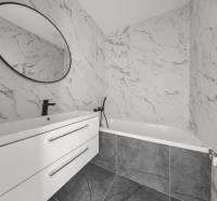 Badezimmer in einer 2-Zimmer-Wohnung mit Badewanne, weißem Waschbecken und rundem Spiegel.