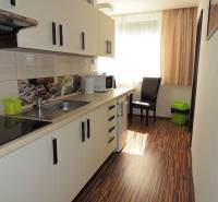 Küche in einer 2-Zimmer-Wohnung mit weißen Schränken, Holzboden und einem Fenster mit Rollläden.