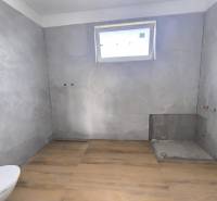 Ein Badezimmer in einem Einfamilienhaus mit Fliesen, bereit zur Installation, Licht durch ein kleines Fenster.