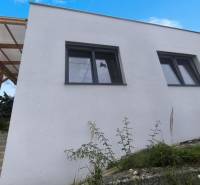 Ein Einfamilienhaus in Malé Kršteňany mit zwei großen Fenstern und einem hölzernen Unterstand.