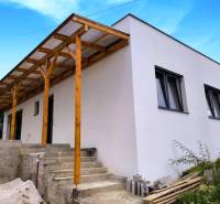 Ein Einfamilienhaus in Malé Kršteňany mit einem Holzvorbau und Betontreppen, blauer Himmel.