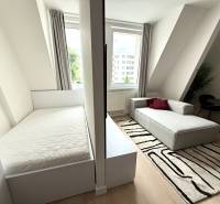Garsónka mit einem hellen Bett, einem grauen Sofa und einem schwarz-weißen Teppich.