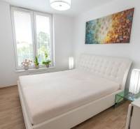 Schlafzimmer in einer 3-Zimmer-Wohnung mit großem Bett, Bild und Blumen auf der Fensterbank.