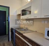Küche in einem Einzimmerapartment mit weißer und hölzerner Küchenzeile, Mikrowelle und Esstheke.