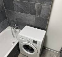 Ein Badezimmer in einer 4-Zimmer-Wohnung mit Badewanne und Waschmaschine in dunkelgrauen Fliesen.
