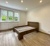 Helles Schlafzimmer mit Holzbett in einer 2-Zimmer-Wohnung mit großen Fenstern.