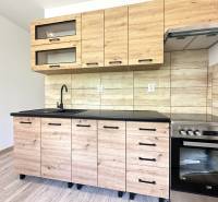 Küche mit Holzverkleidung in einer 2-Zimmer-Wohnung, ausgestattet mit Glasschränken und Herd.