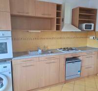 Küche mit Holzschränken, gelben Fliesen und eingebauten Geräten in einer 2-Zimmer-Wohnung.
