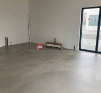 Ungeordnete Geschäftsräume mit großen Fenstern und Betonboden.