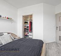 Schlafzimmer mit Bett im Einfamilienhaus, offener Kleiderschrank und Regal mit Parfums.