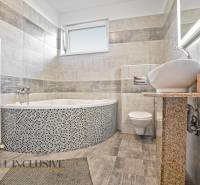 Ein Badezimmer in einem Einfamilienhaus mit Badewanne, Waschbecken und Toilette, gefliest mit hellen Fliesen.