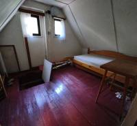 Ein Zimmer im Obergeschoss einer Hütte mit einem Boden in Holzoptik, einfacher Einrichtung und Fenstern.