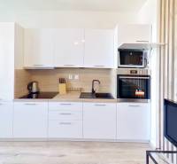 Küche in einer Einzimmerwohnung mit weißer Küchenzeile, Herd, Backofen und offener Balkontür.