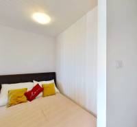Schlafzimmer mit Doppelbett, weißen Wänden und bunten Kissen in einer Einzimmerwohnung.