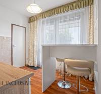 Küche in einer 2-Zimmer-Wohnung mit Bartresen, Vorhängen und hellen Möbeln.