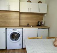 Küche in einer Einzimmerwohnung mit weißen Schränken, Waschmaschine, Spüle und Esstisch.