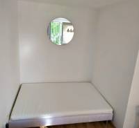 Ein Bett, ein rundes Spiegel und Holzboden in einer Einzimmerwohnung.