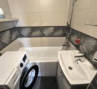 Badezimmer in einer 2-Zimmer-Wohnung mit Waschmaschine, Badewanne, Waschbecken und dekorativen Fliesen.